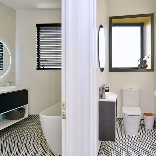 Modern bathroom with black and white tiled floor, featuring a tub, toilet, and vanity.