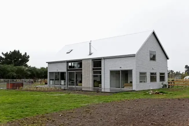 Modern white house with a silver roof on a grassy field under a cloudy sky.