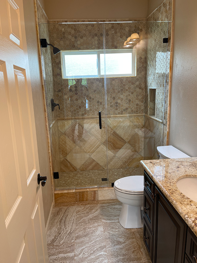Bathroom with glass shower, beige and brown tile, toilet, dark wood vanity, and window.