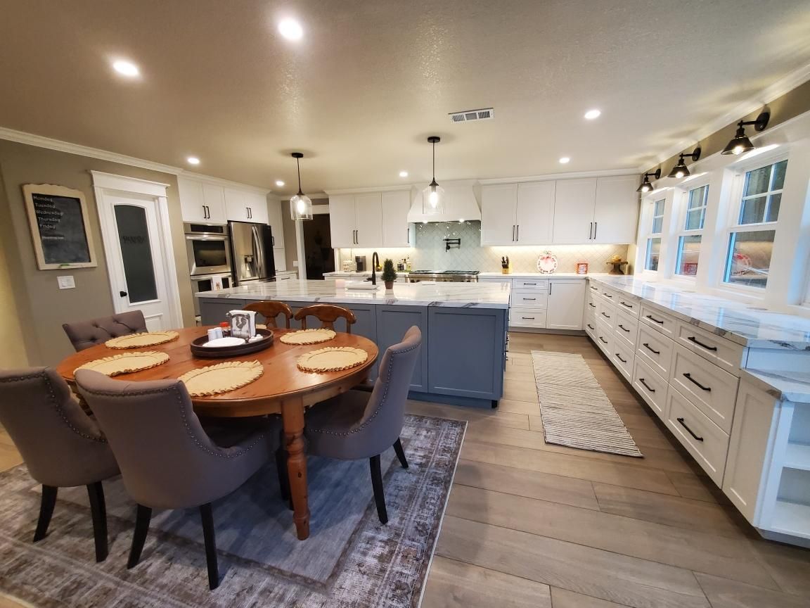 Spacious kitchen with a round dining table, gray island, white cabinets, and wood flooring.