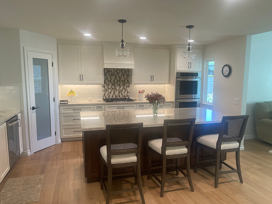 Modern kitchen with an island, pendant lights, white cabinets, and wooden floors.