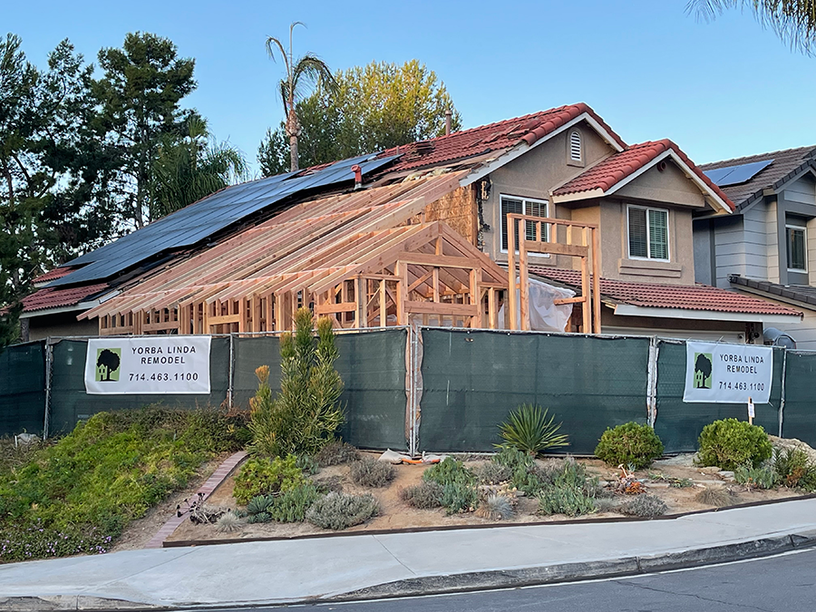 House under construction with exposed wooden frame, surrounded by a green fence.