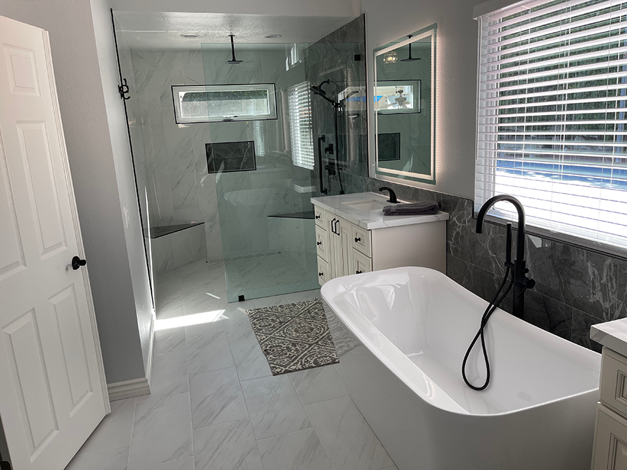Modern bathroom: white soaking tub, glass shower, vanity, marble tile, window with blinds.