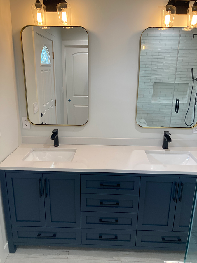 Navy blue double vanity with two mirrors, black faucets, and warm lighting.