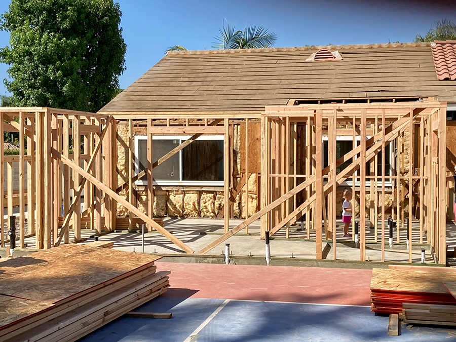 Wood framing of a house addition under construction; a window and a child are visible.