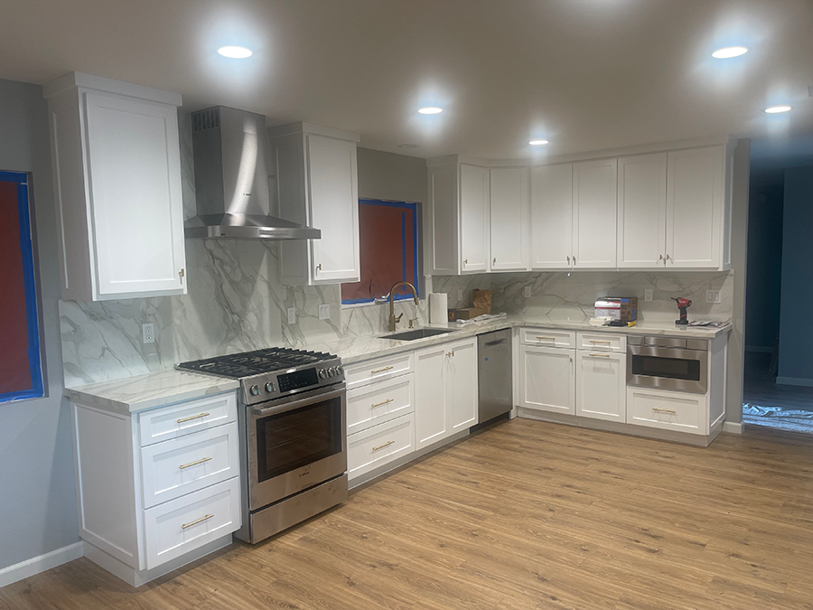 A modern kitchen with white cabinets, stainless steel appliances, and wood-look flooring.