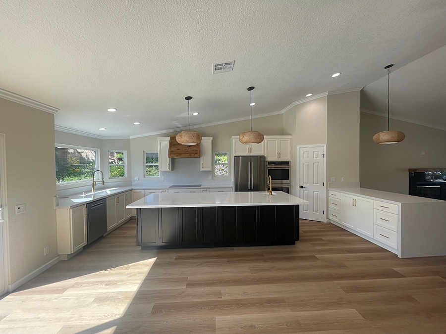 Spacious kitchen with a black island, white cabinets, and wood pendant lights over a light wood floor.