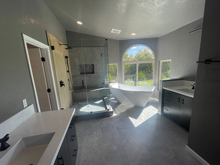 Spacious modern bathroom with large windows, a standalone tub, and a glass shower. Gray walls and dark cabinets.