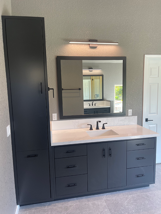 Dark gray bathroom vanity and tall cabinet with white countertop, black fixtures, and large mirror.