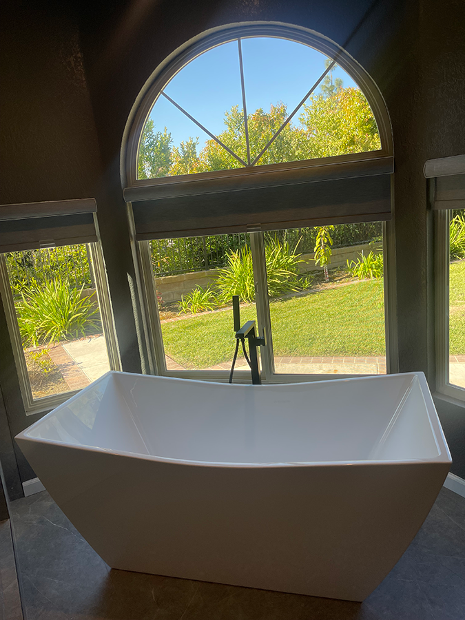 White freestanding bathtub in front of large window overlooking a grassy backyard.