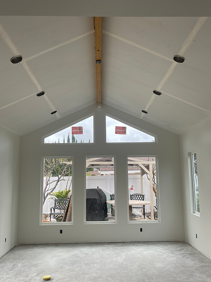 Interior of a room with a high, angled ceiling, windows, and recessed lighting. Drywall and exposed beams visible.