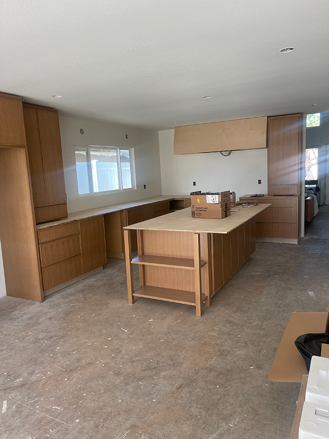 Kitchen under construction with light wood cabinets and island, white walls, and concrete floor.