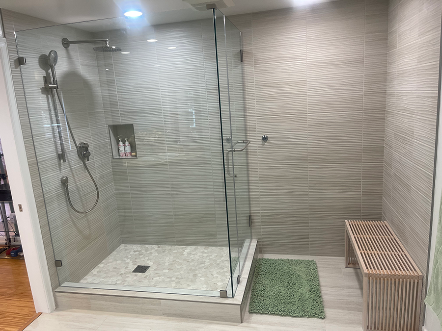 Modern bathroom with glass shower, textured gray tile, and wooden bench.