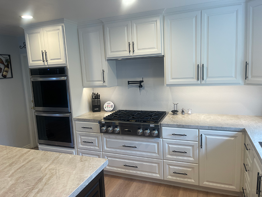 White kitchen with double ovens, stovetop, cabinets, and light-colored countertops.