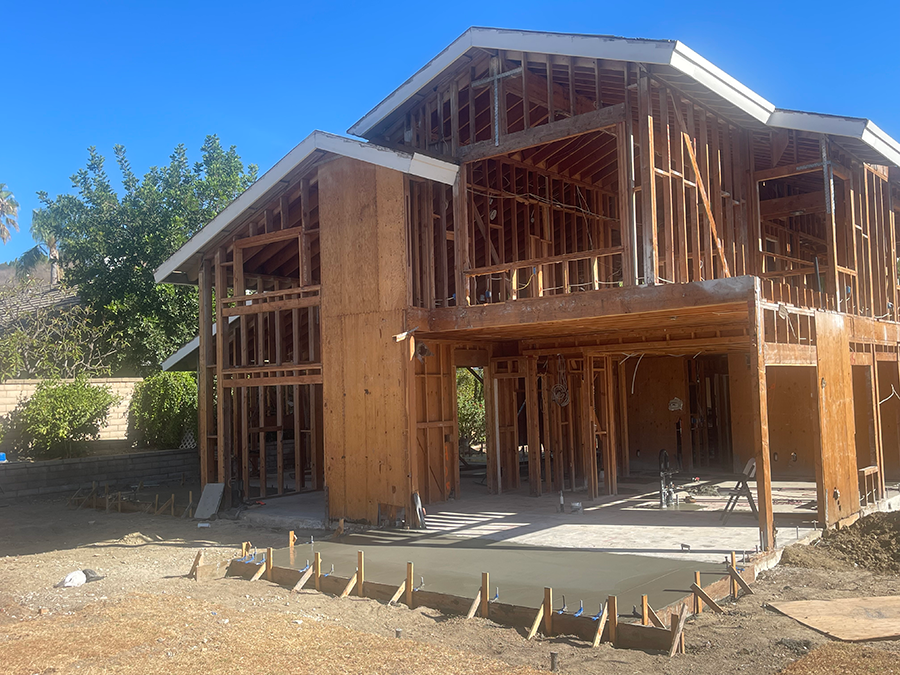 Two-story house under construction with exposed wooden framing and a concrete slab.