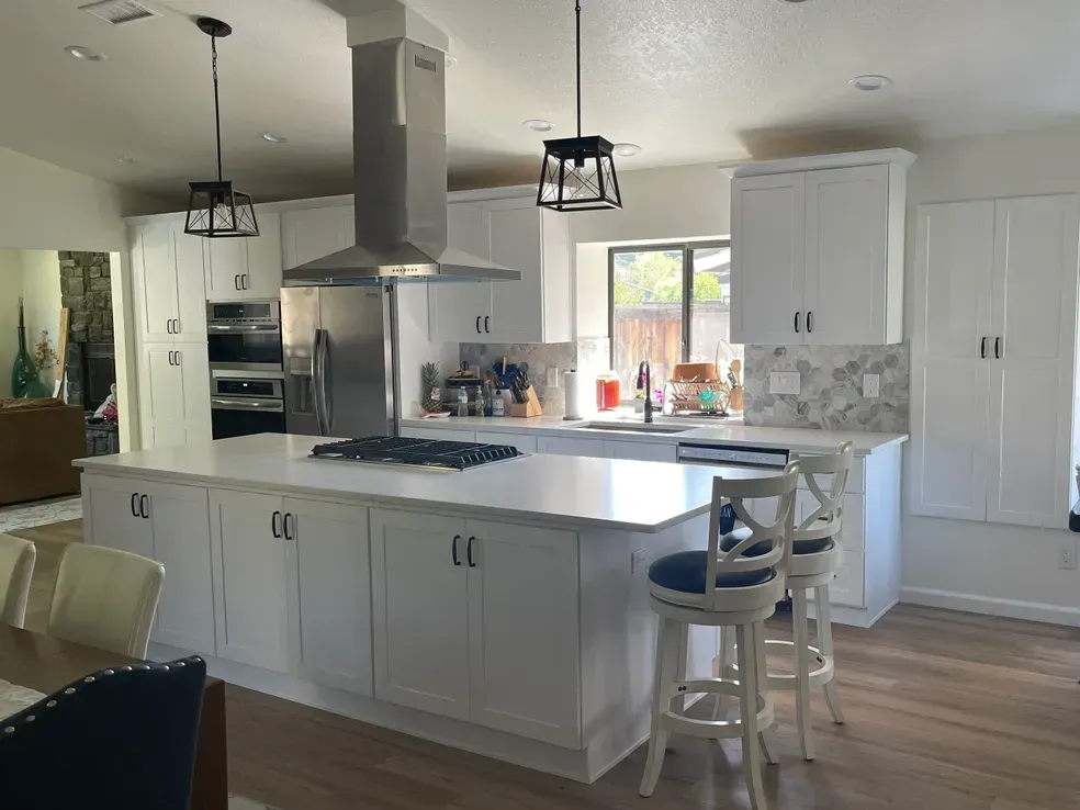 Bright white kitchen with island, stainless steel vent hood, and marble backsplash.