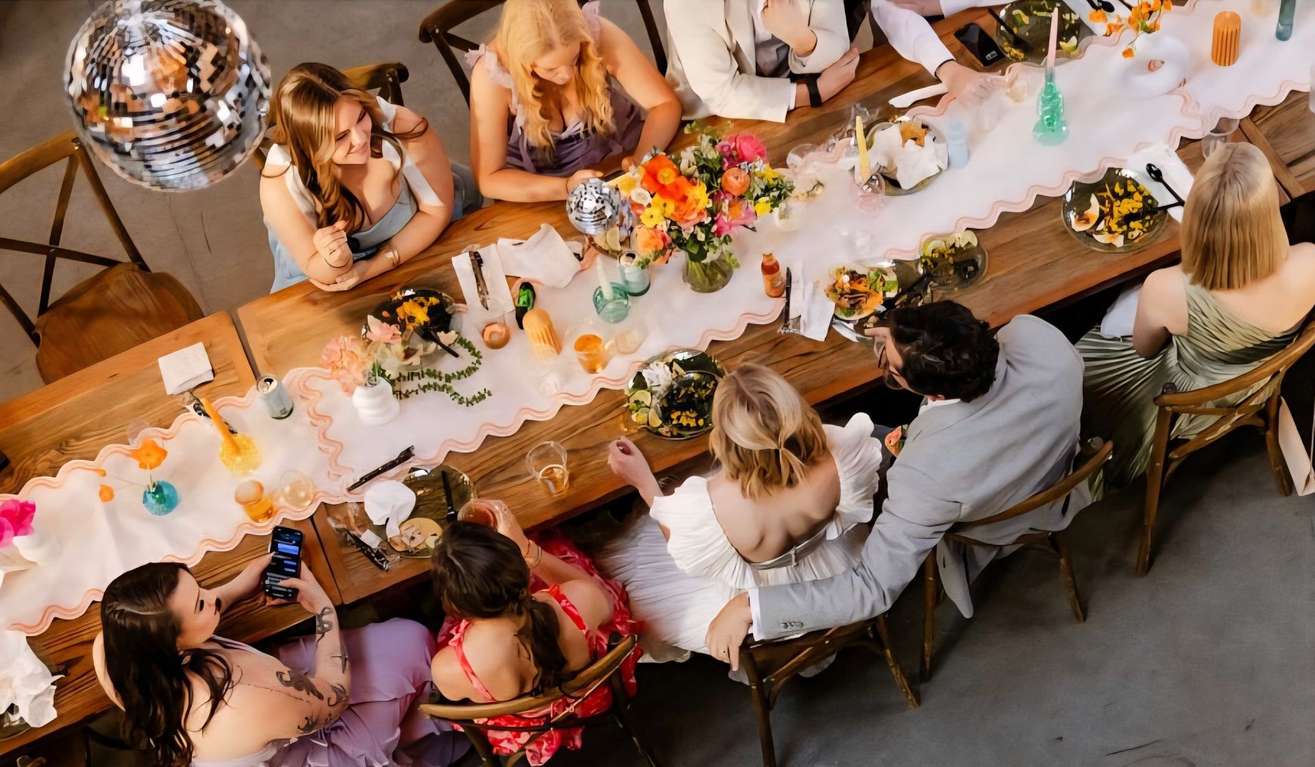 bride and groom dining with guests at long reception table with colorful, whimsical centerpieces