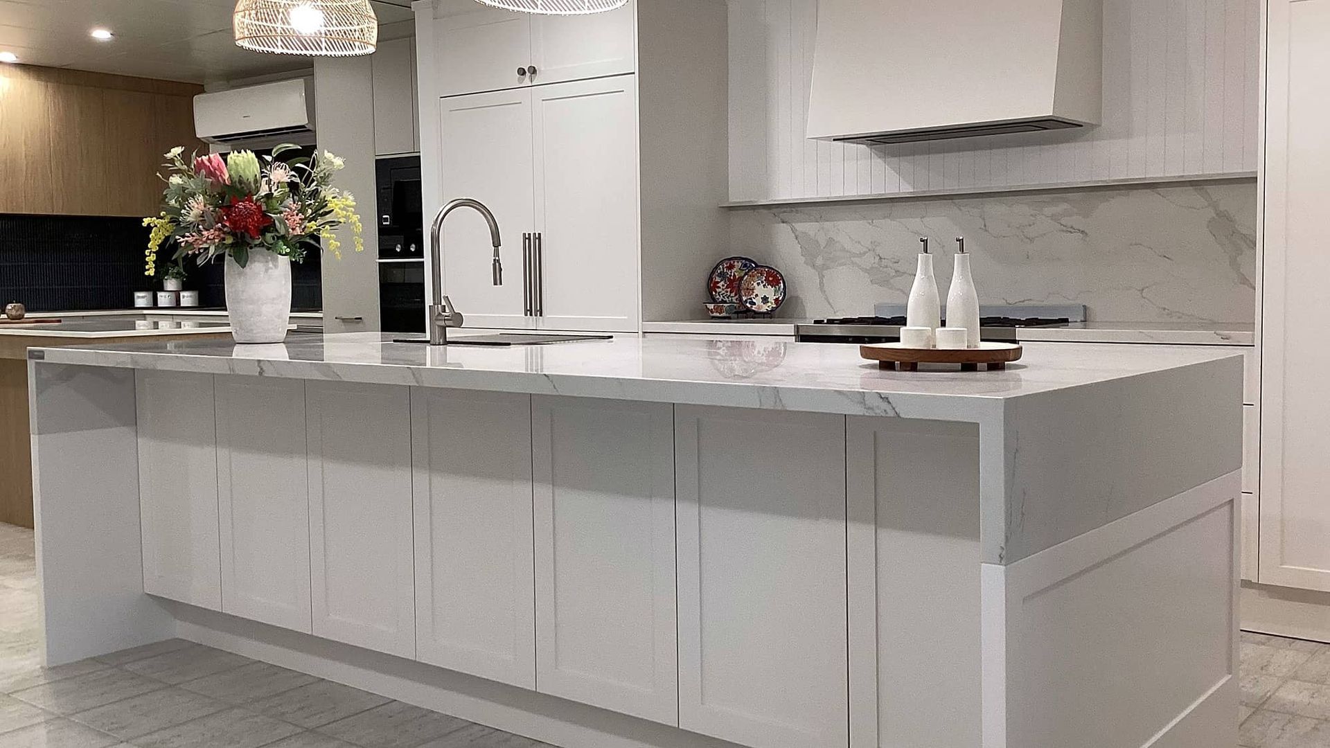 A Kitchen With White Cabinets and a Large Island With a Vase of Flowers on It — Kenross Kitchens In Gosford, NSW