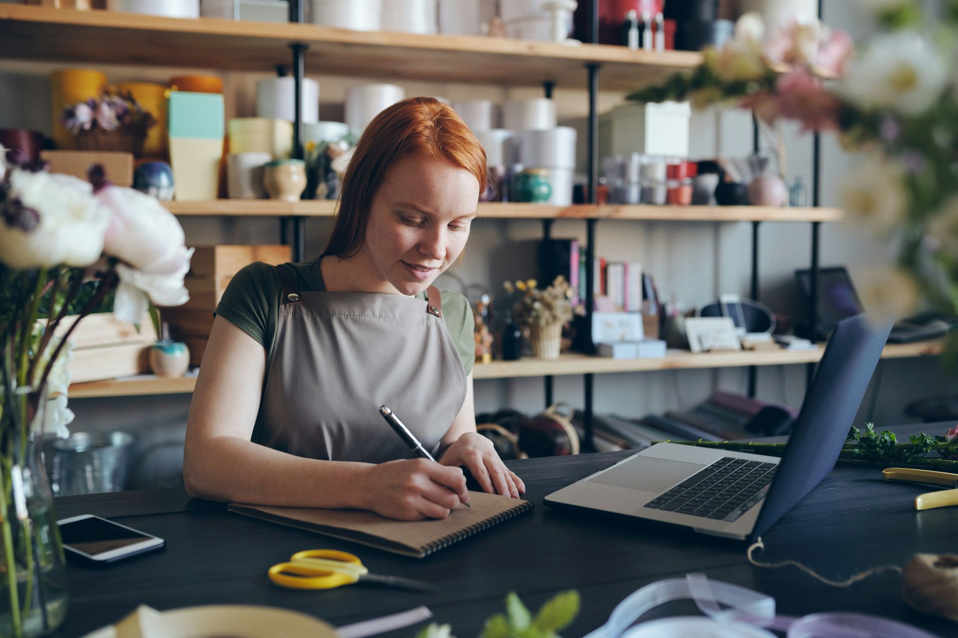 Hand with gold wedding ring on a wooden surface, blurred outdoor background.