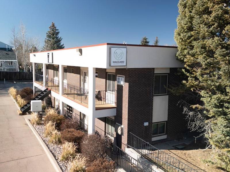 Man in navy suit and tie smiling. Against a gray background.