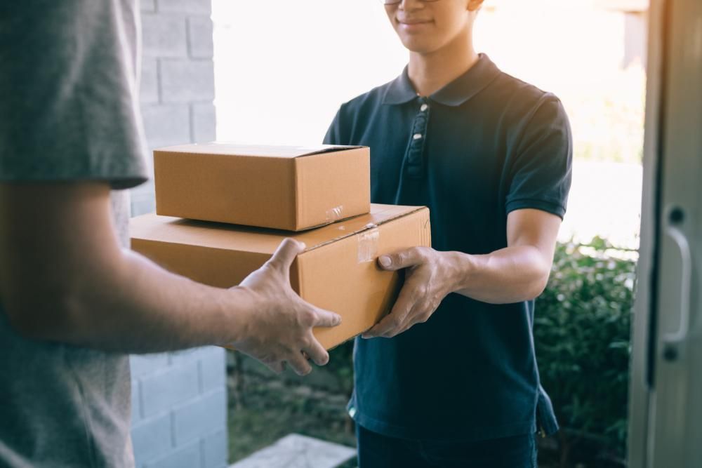 A Delivery Man Is Handing A Package To A Customer — Geurie General Store In Geurie, NSW