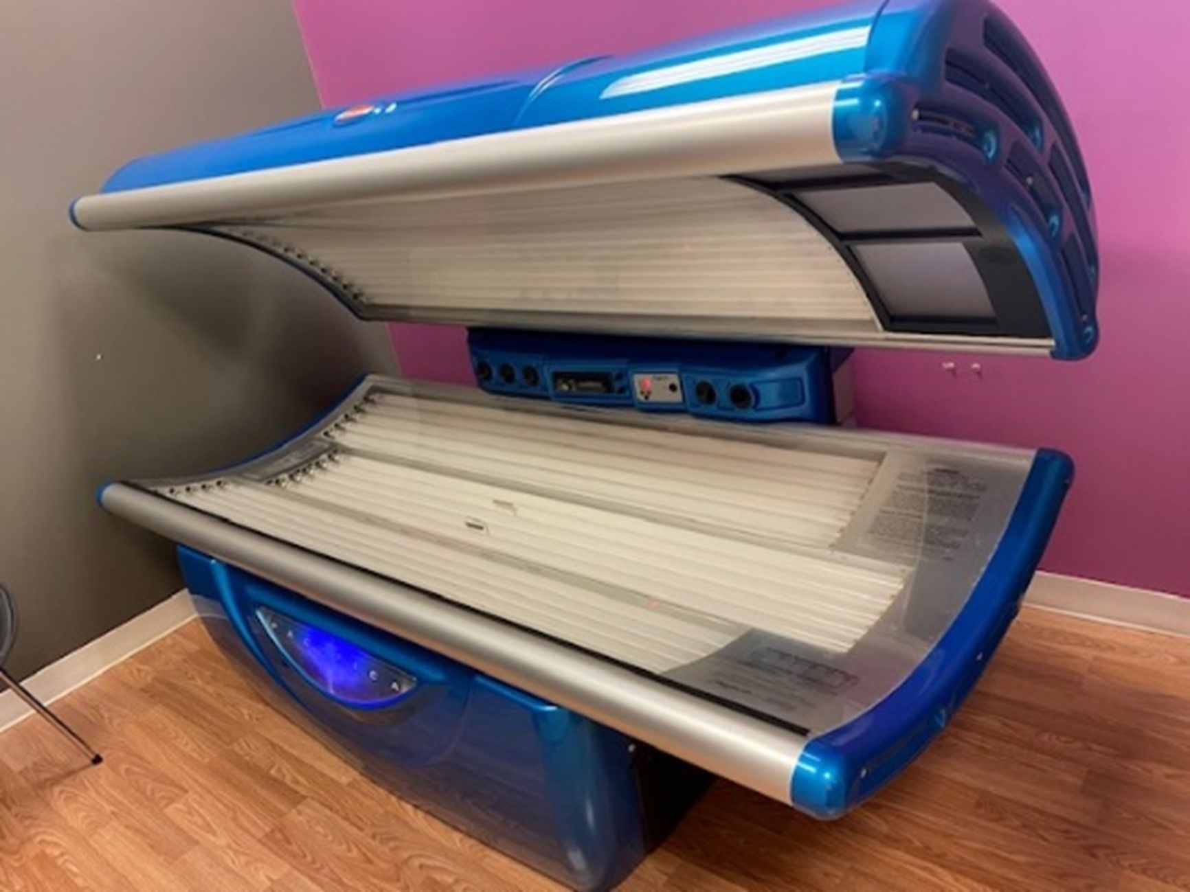 A blue and silver tanning bed in a room with wood flooring and purple and grey walls.