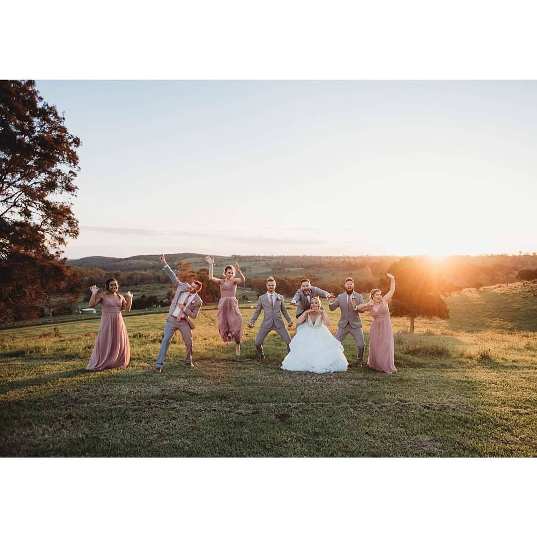 A bride and her wedding party are posing for a picture in a field.