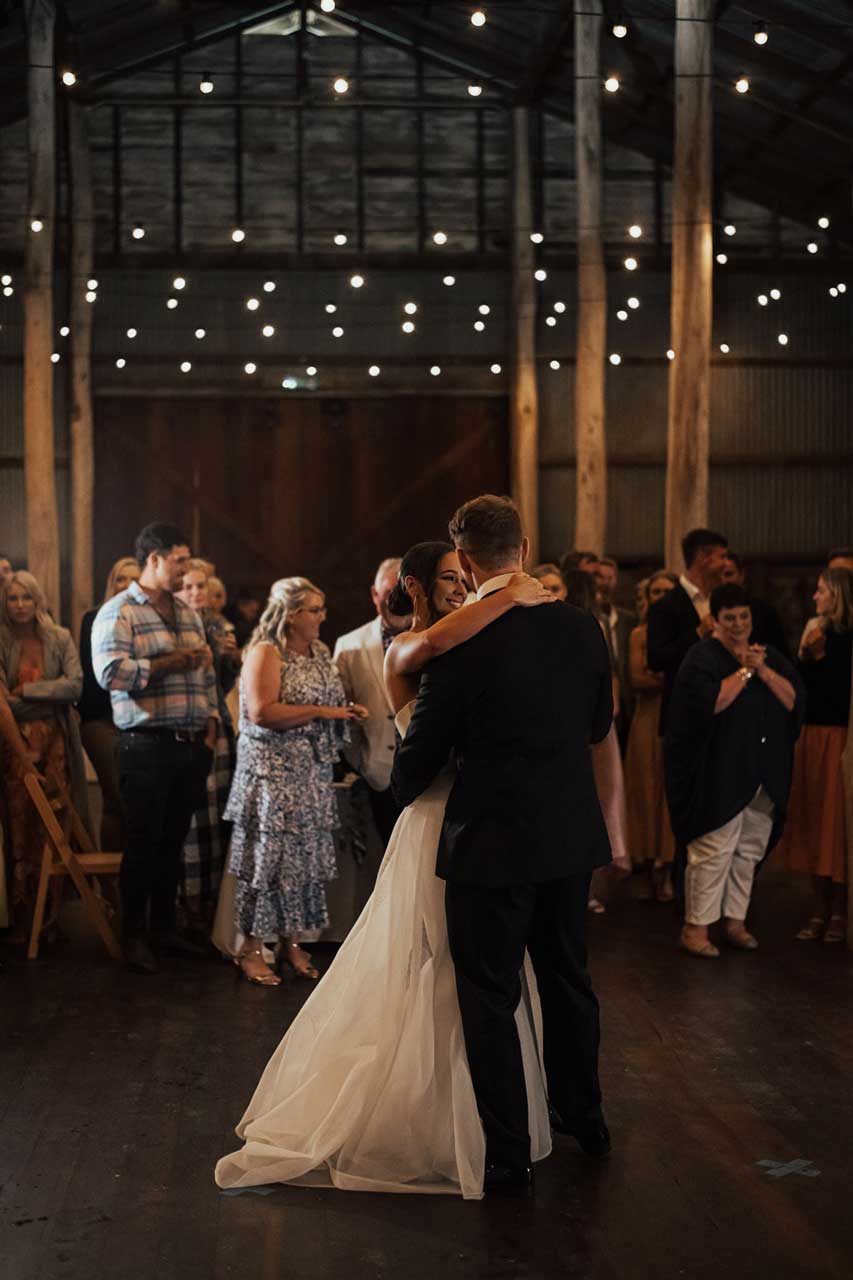 A bride and groom are dancing at their wedding reception in a barn.