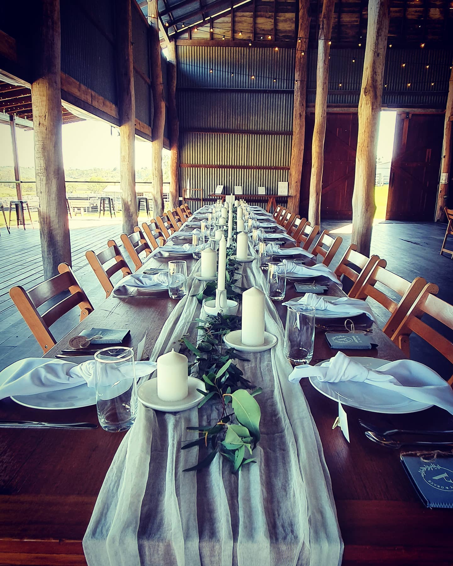 A long wooden table with plates , glasses , and candles on it.