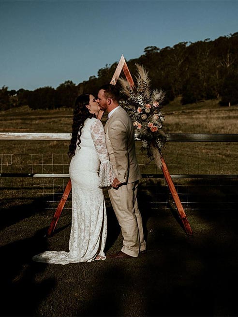 A bride and groom are kissing under a wooden arch.