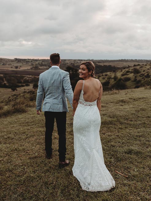 A bride and groom are standing in a field holding hands.