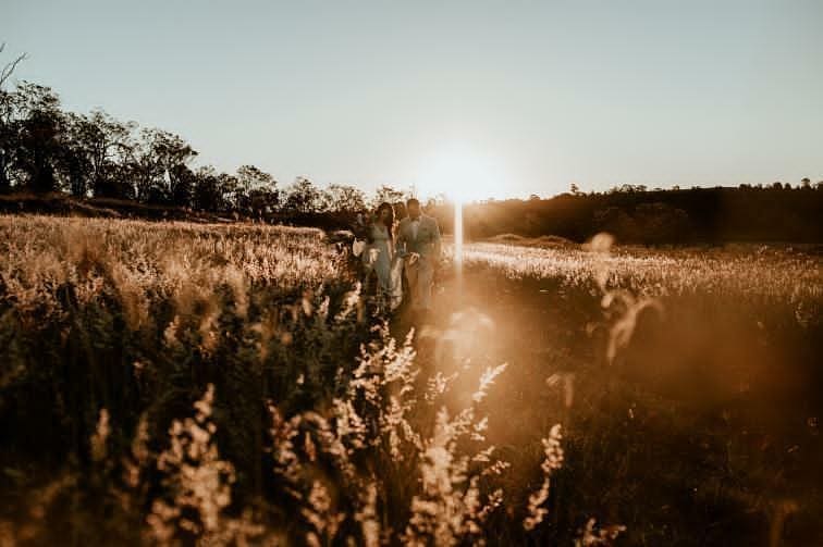 A couple is walking through a field of tall grass at sunset.