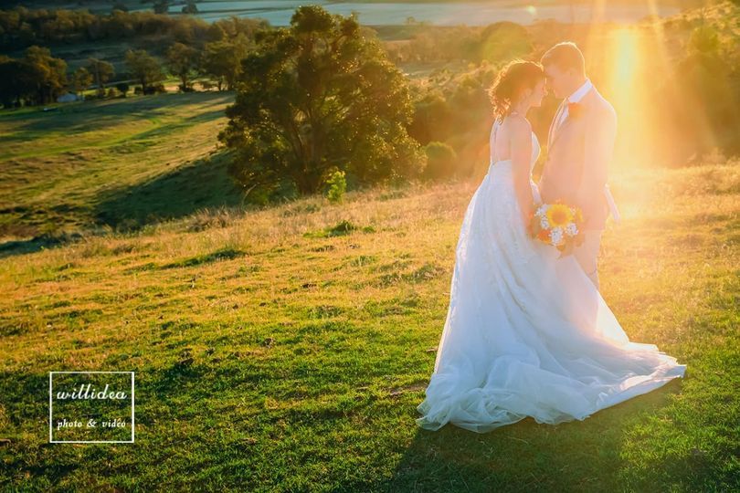 A bride and groom are kissing in a field at sunset.
