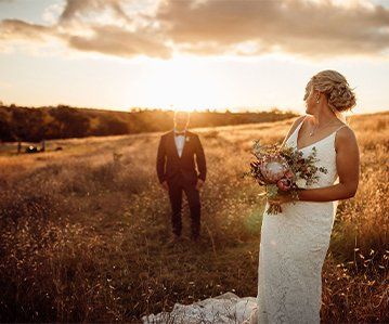 A bride and groom are standing in a field at sunset.