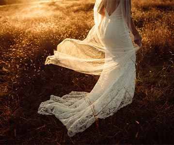 A woman in a white lace dress is standing in a field.