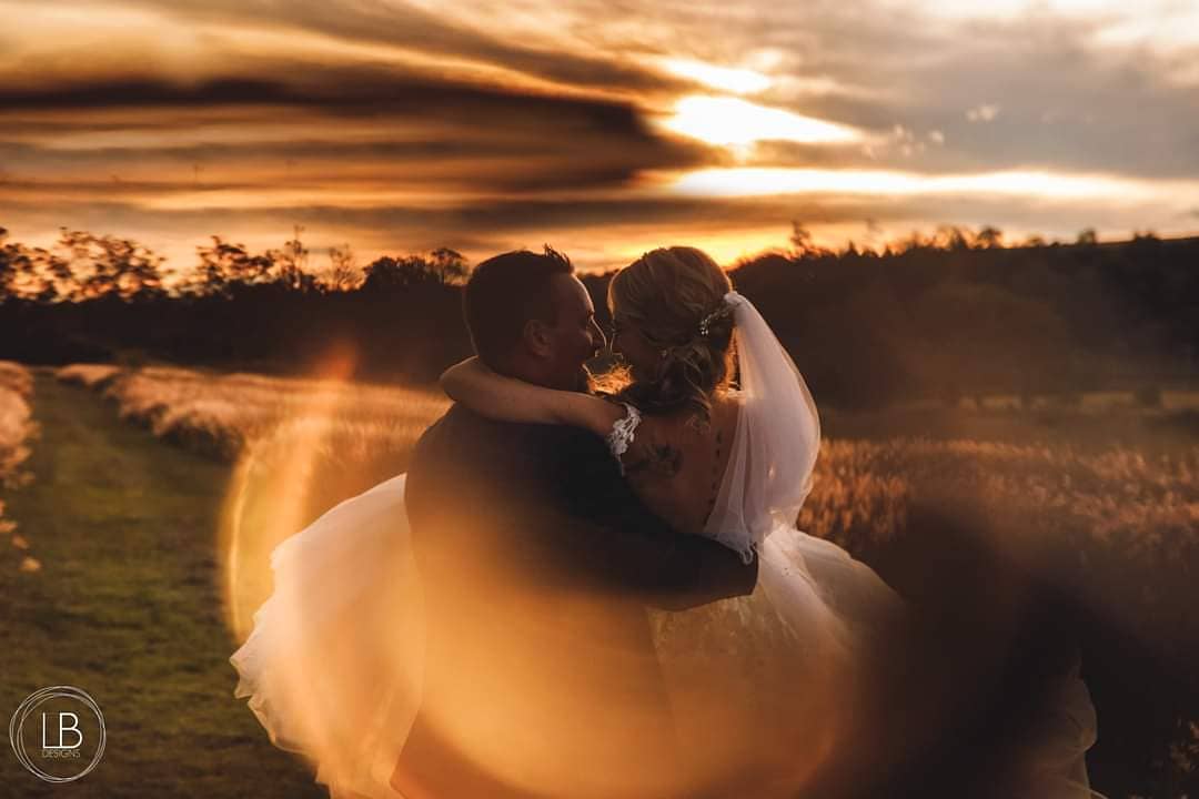 A bride and groom are kissing in a field at sunset.