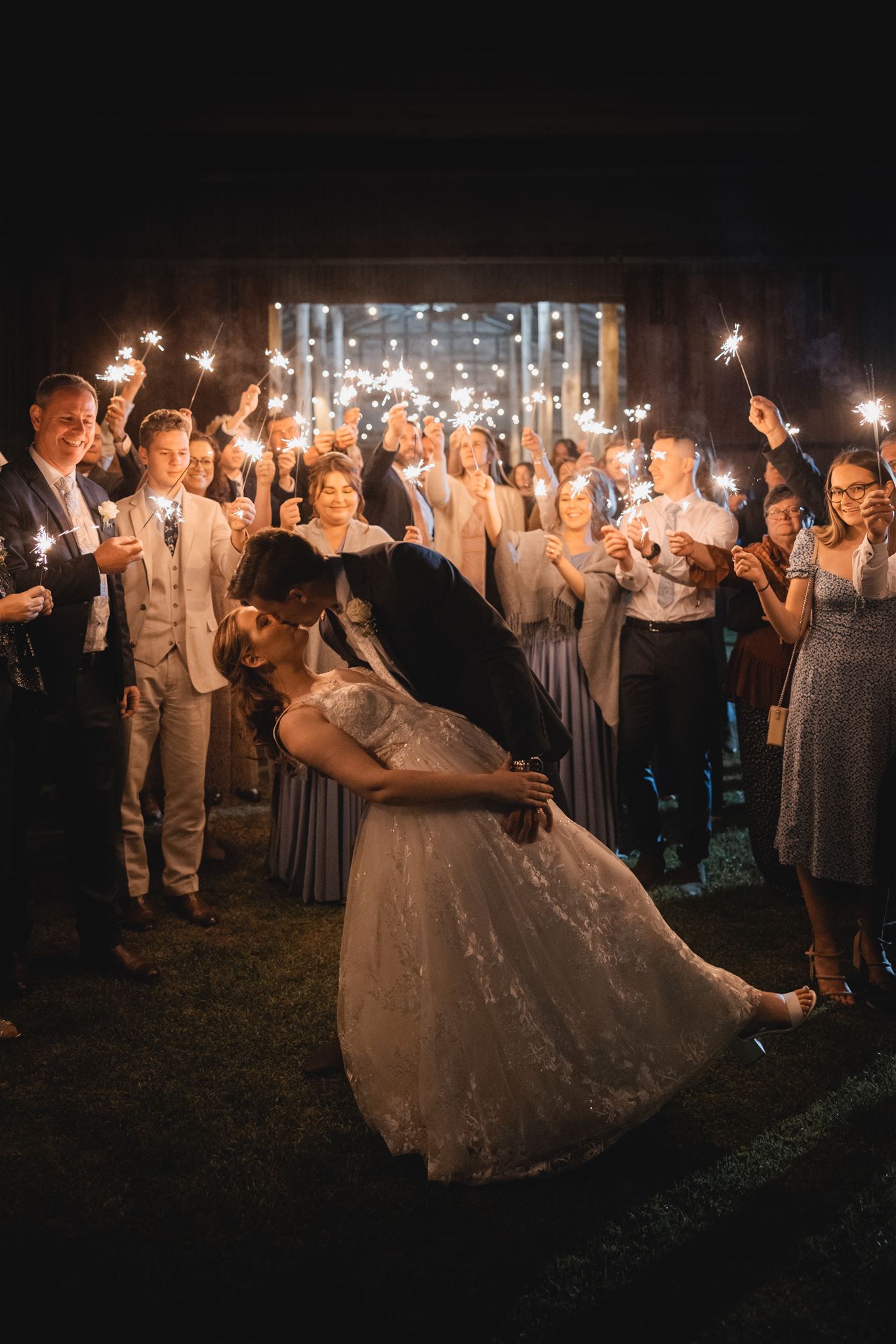 A bride and groom are kissing in front of a crowd of people holding sparklers.