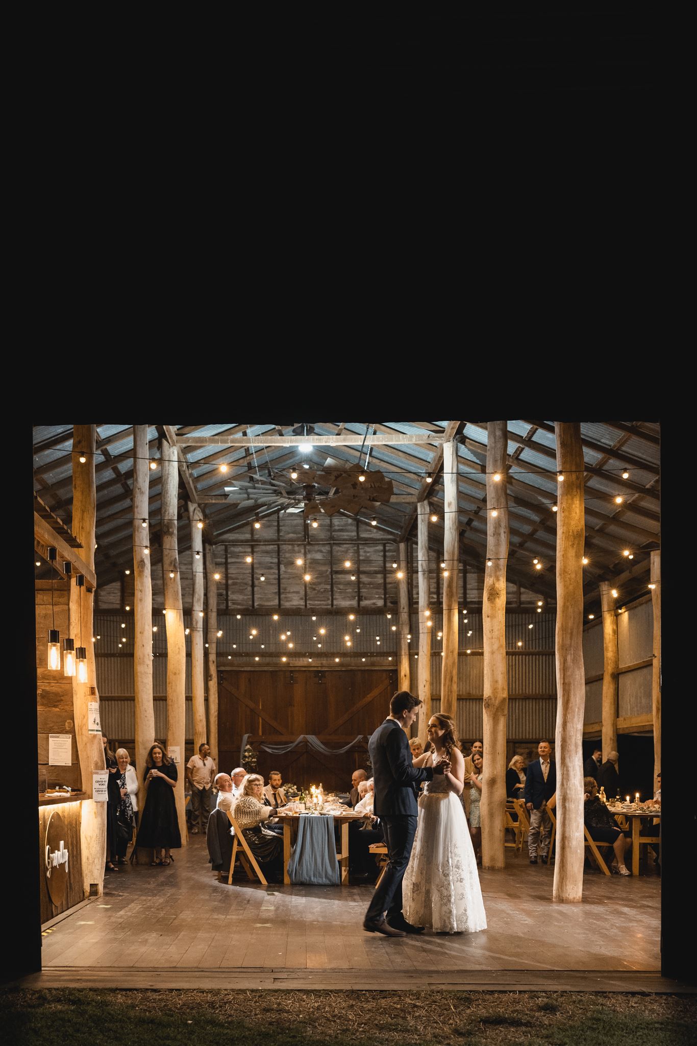 A bride and groom are dancing in a barn at their wedding reception.