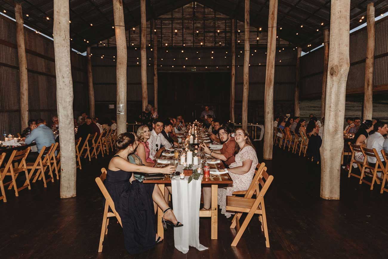 A group of people are sitting at a long table in a barn.