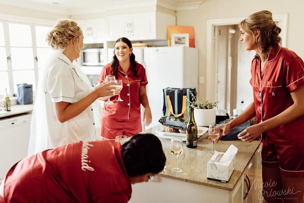 A group of women are standing around a kitchen counter drinking wine.