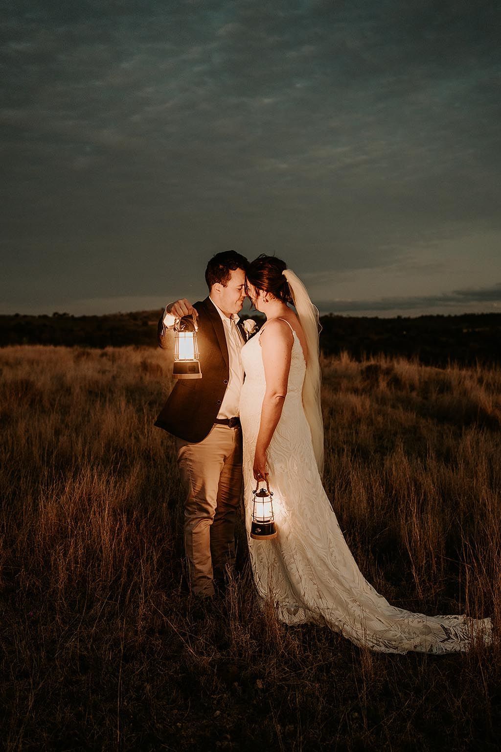 A bride and groom are standing in a field holding lanterns.