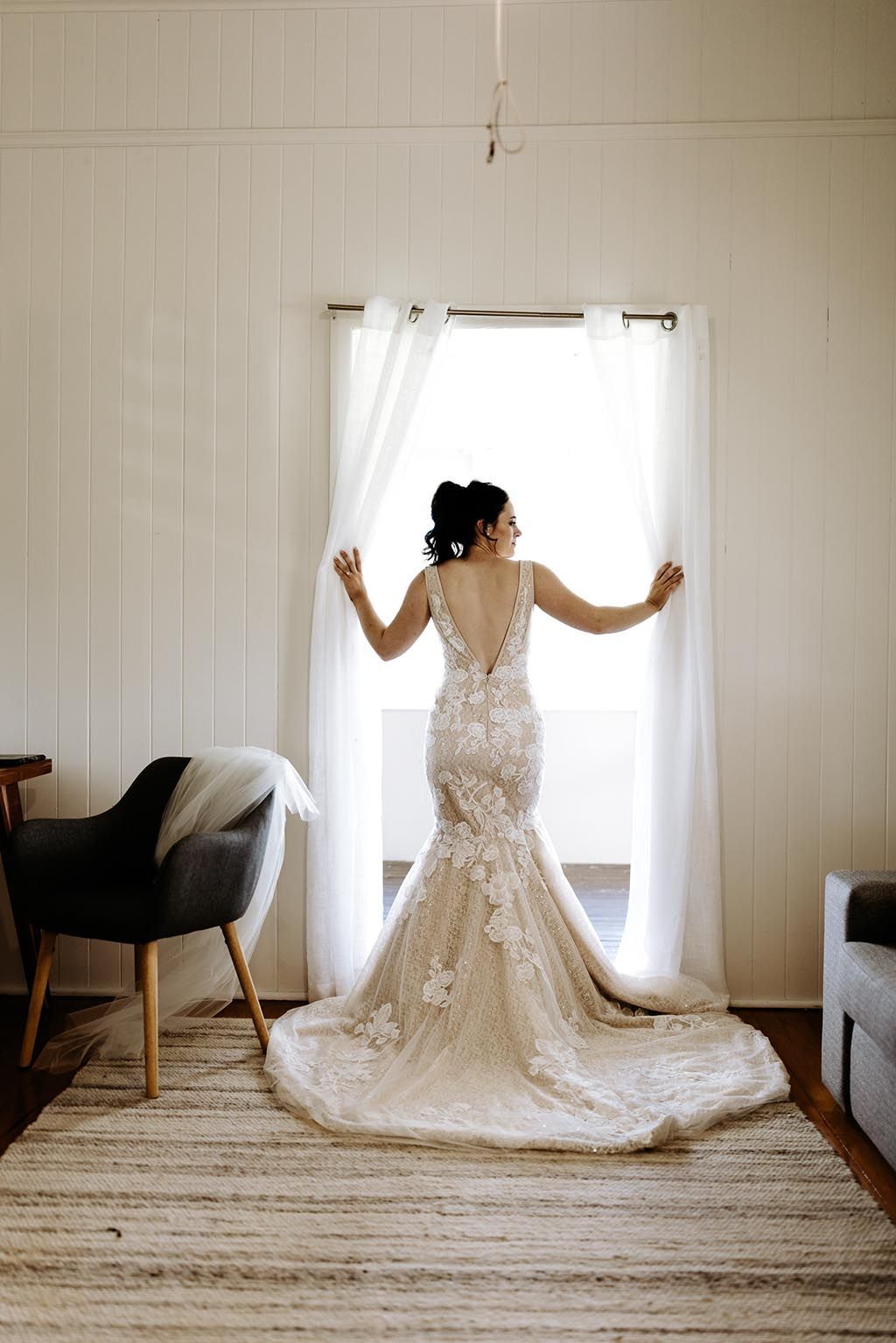 A woman in a wedding dress is standing in front of a window.