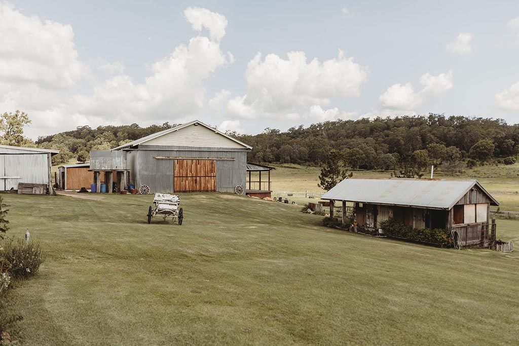 A car is parked in a grassy field in front of a barn.