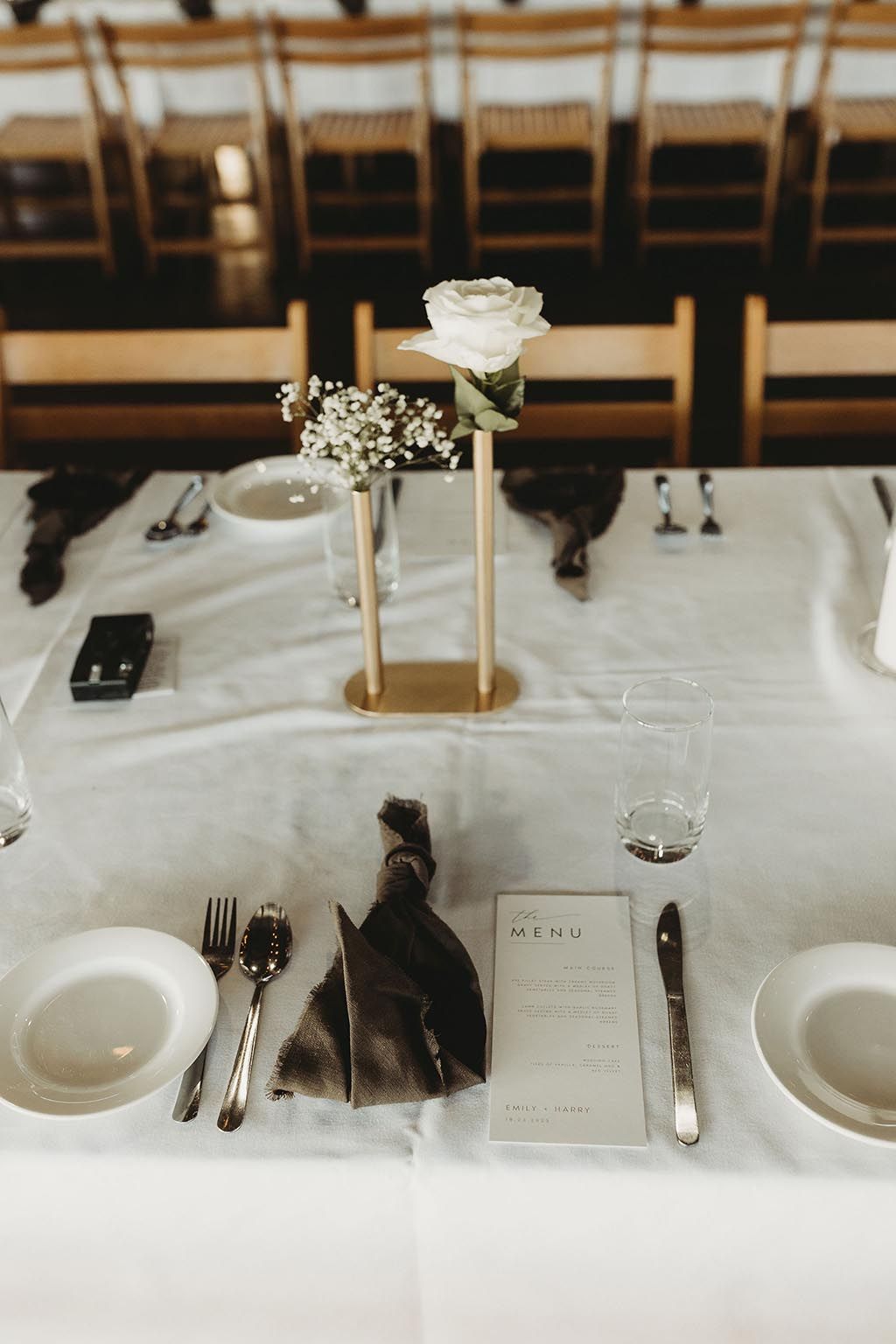 A table with plates , utensils , a menu and a vase of flowers on it.