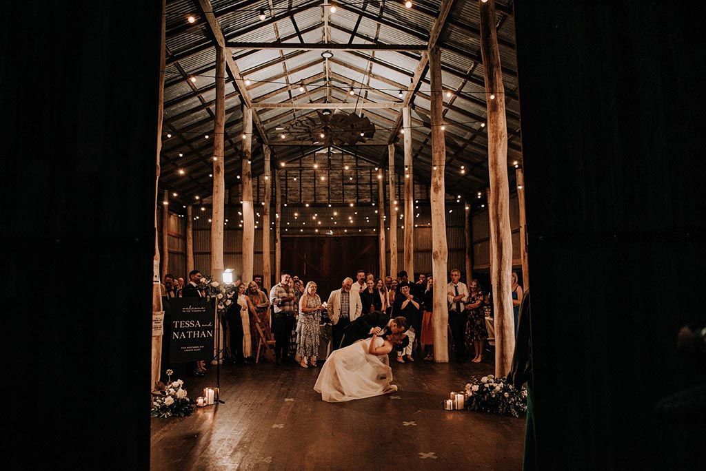 A bride and groom are dancing in a barn at their wedding reception.