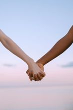 Two people holding hands, with light and dark skin tones, against a pink and blue sky.