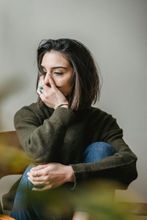 Woman with dark hair, wearing a green sweater, covering her face while sitting.