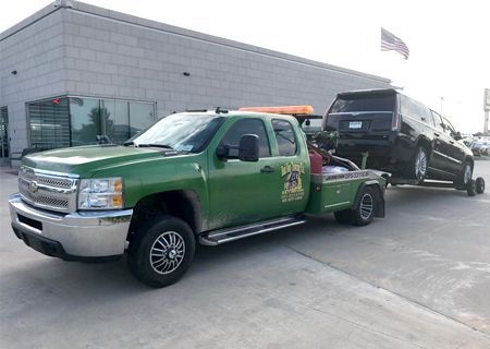Green tow truck towing a black SUV in front of a building.