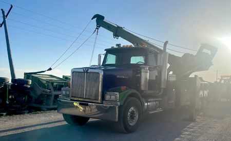 Tow truck lifting a green farm implement under a bright blue sky.