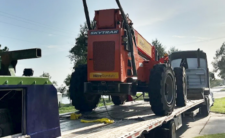 Orange SkyTrak telehandler on a flatbed trailer, ready for transport.
